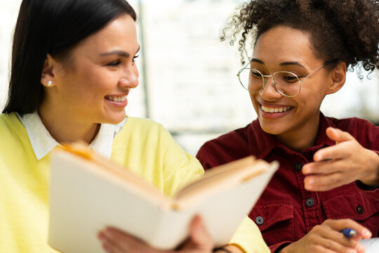 Two teen schoolgirls working on the project together at the library. Women reading book. Studying, learning concept