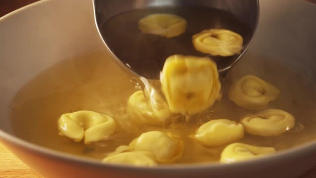 Pour a ladle of tortellini pasta soup. Hot soup dish is on table. Typical italian recipe for lunch and dinner. Cozy soup with meat broth and stuffed pasta, hot and cozy soup for dinner at home. 