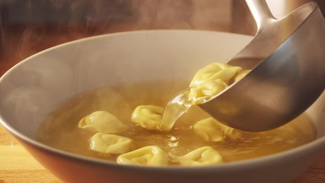 Pour a ladle of tortellini pasta soup. Hot soup dish is on table. Typical italian recipe for lunch and dinner. Cozy soup with meat broth and stuffed pasta, hot and cozy soup for dinner at home. 