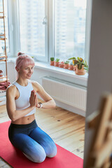 Sportswoman in tracksuit meditates with namaste mudra sitting on knees on balcony
