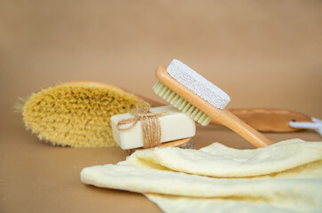 A wooden brush for dry body massage and natural soap lie on a towel. Foot brush and pumice stone for heels.