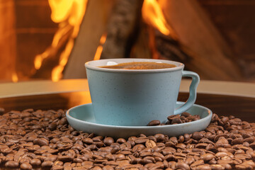 A cup of coffee and coffee beans on a background of burning fireplace.