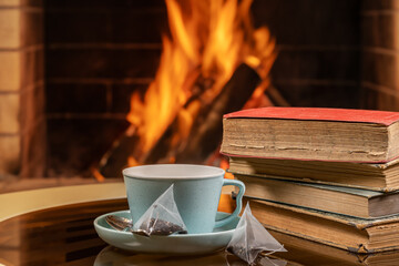 A cup of tea and old books on a background of burning fireplace.