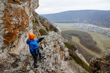 Portrait of brave boy on a rock and looks ahead. Rock climbing and climbing uphill at a young age....
