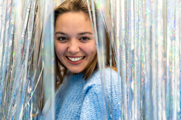 Portrait of an attractive and elegant young woman looking at the camera between a curtain of glitter and silver and colored reflections