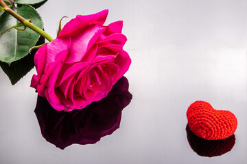 pink rose and knitted heart on black mirror background