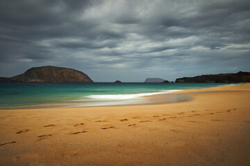 Fototapeta premium landscape of an idyllic beach with turquoise waters with several islands in the sea and some footprints in the sand in the foreground, clouds in the sky