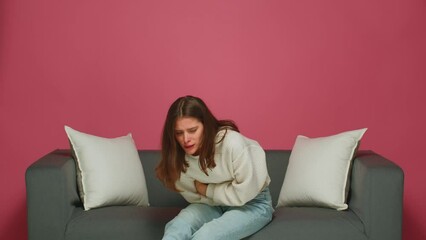 Sick young girl suffer stomachache, sitting on sofa. Diarrhea, indigestion, poisoning or painful periods