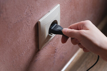 A woman's hand inserts an electric plug into a socket, close-up