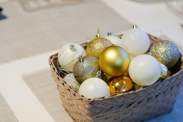 A basket with white, silver and gold New Year's tree balls on the table. Christmas decorations and festive bright decor. Sparkle background. Joy and fun. Family time.