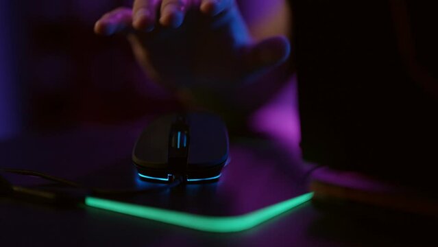 Close-up hands of gamer playing video game using illuminated mouse.Male hand using mouse. Background with neon lights.