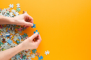 Female hands collect scattered puzzles on a yellow background close-up, top view, copy space. Board games, hobby, leisure