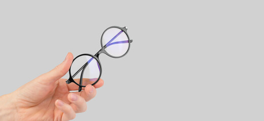 Round stylish glasses for vision in a male hand on a gray background, copy space