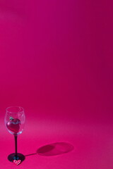 Heart as an expression of love in a wine glass on a red background with a shadow of glass and copy space. Minimalistic romantic scene.
