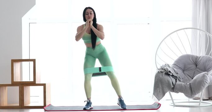 Resistance band fitness girl in green sportswear doing leg workout floor exercises with rubber strap elastic.