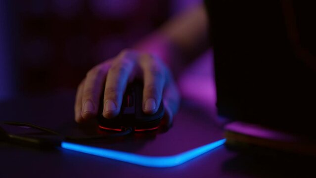 Close-up hands of gamer playing video game using illuminated mouse.Male hand using mouse. Background with neon lights.