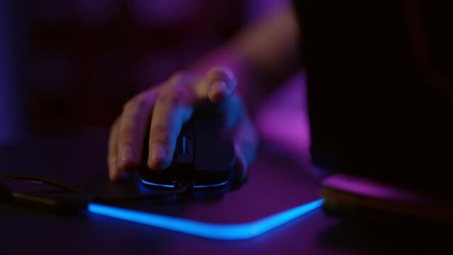 Close-up hands of gamer playing video game using illuminated mouse.Male hand using mouse. Background with neon lights.