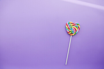 Rainbow colorful heart shaped candy on purple background with shadows. Copy space. Minimalist concept.