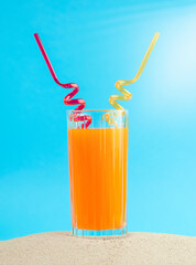 Summer concept. Orange cocktail with two straws on the sand.