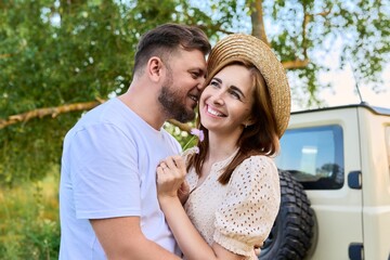 Happy hugging man and woman near car, summer nature wild meadow background