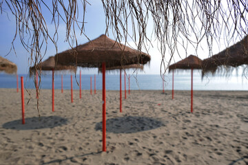 Typical straw beach umbrella in province of Malaga, Andalusia, Spain. Straw beach umbrellas in a row, Mediterranean coast, sandy beach, blue sea, horizon.