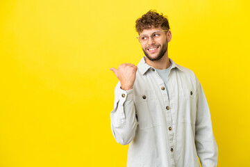 Young handsome caucasian man isolated on yellow background pointing to the side to present a product