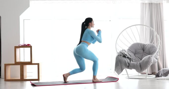 Young fitness woman doing squat exercises with lunges from leg to leg. Fit Female is a workout at home in the living room.