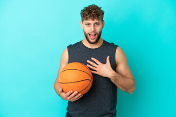 Handsome young man playing basketball isolated on blue background surprised and shocked while looking right