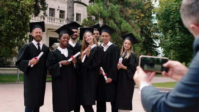 Graduation day in the college park group of multiracial graduates students posing excited with diplomas in front of the smartphone the college principal taking pictures