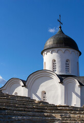 Close-up of the view from the stone wall to the upper part of the Orthodox church. White stone single-domed church. Blue sky with clouds. Daylight.