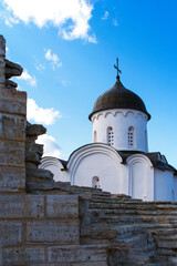 View from the stone wall on the upper part of the Orthodox church. White stone single-domed church. The corner of the wall. Blue sky with clouds. Daylight.