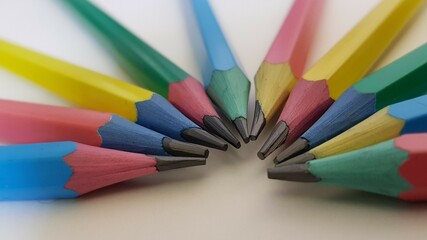 A selection of blue, yellow, pink and green hexagon shaped pencils with colored erasers fanned out with the sharpened graphite together.