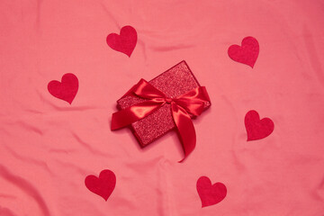 Red gift box with red bow and hearts around on pink silk background. Valentine day concept