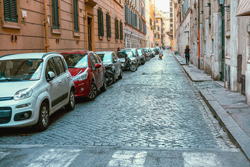 narrow cobbled street with many parked small cars in the historic part of the Italian capital