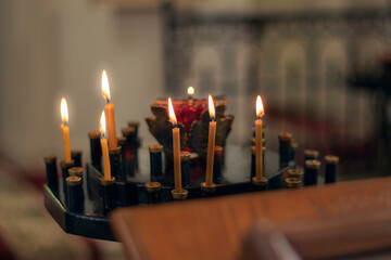 Burning candles in a black church candlestick. Blurred background and foreground. There is a blurred wooden pedestal in the foreground. Close-up.