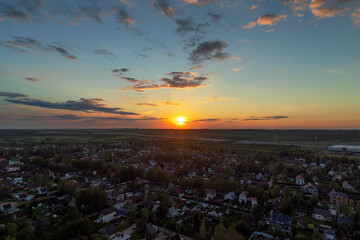 View from the height of a large village in the background of sunset. The motorway is visible in the distance. High-rise buildings are visible in the distance. There are few clouds in the sky. Summer.