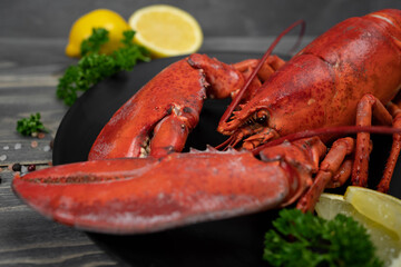 Lobster decorated with lemon slices on black plate on wooden table. Fresh seafood.