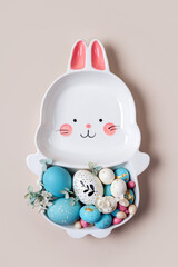 Happy Easter concept. Cute plate in the shape of a bunny with  Easter eggs and candy on beige background.