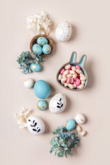 Easter eggs with candy and flowers on beige. Happy Easter concept. White and blue eggs with cute...