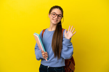 Student kid woman over isolated yellow background saluting with hand with happy expression