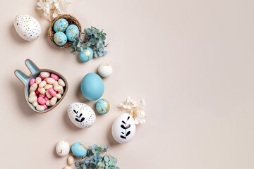 Easter eggs with candy and flowers on beige. Happy Easter concept. White and blue eggs with cute...