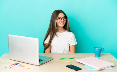 Little girl in a table with a laptop over isolated blue background thinking an idea while looking up