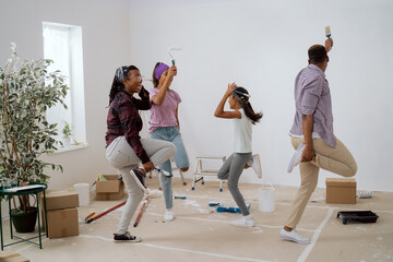 Happy family painting the walls together with white paint in the room dance in the middle of the...