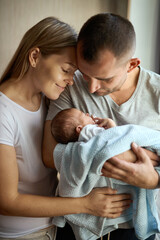 Portrait of young smiling family with newborn on the hands.