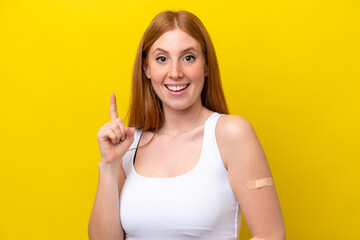 Young redhead woman wearing a band-aids isolated on yellow background pointing up a great idea