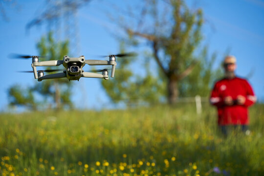 Drone dji air 2s. Modern multicopter over wildflower field. Pilot with red sweater blurred in background.