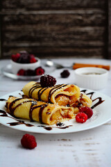 Delicious pancakes with chocolate filling and berries on a white plate on a light background. Vertical