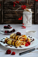Vertical composition. Appetizing pancakes with chocolate filling and syrup on a white plate, raspberries and blackberries on a light background