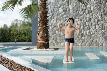 Asian Young Boy Having a good time in swimming pool, He Jumping and Playing a Water in Summer.