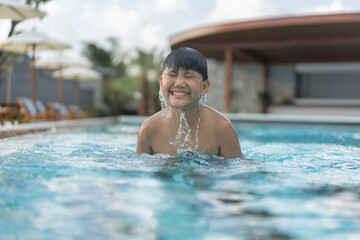 Asian Young Boy Having a good time in swimming pool, He Jumping and Playing a Water in Summer.